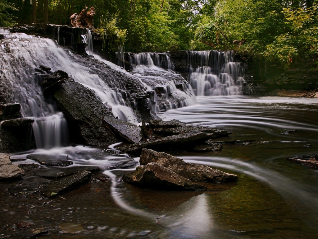 Быстрая вода стекает по камням водопада в парке 