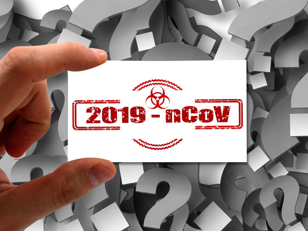 Табличка коронавирус covid-19 в руке на фоне знаков вопроса