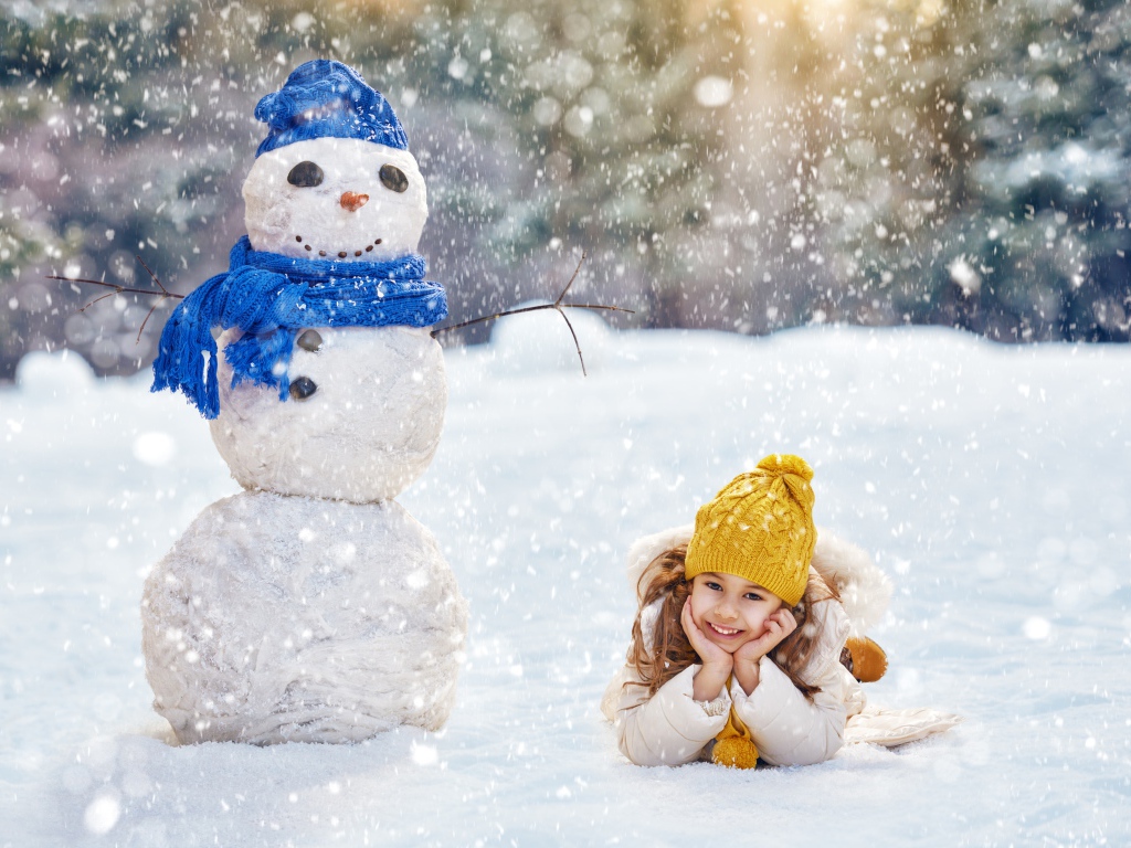 Милая девочка лежит на снегу у снеговика зимой