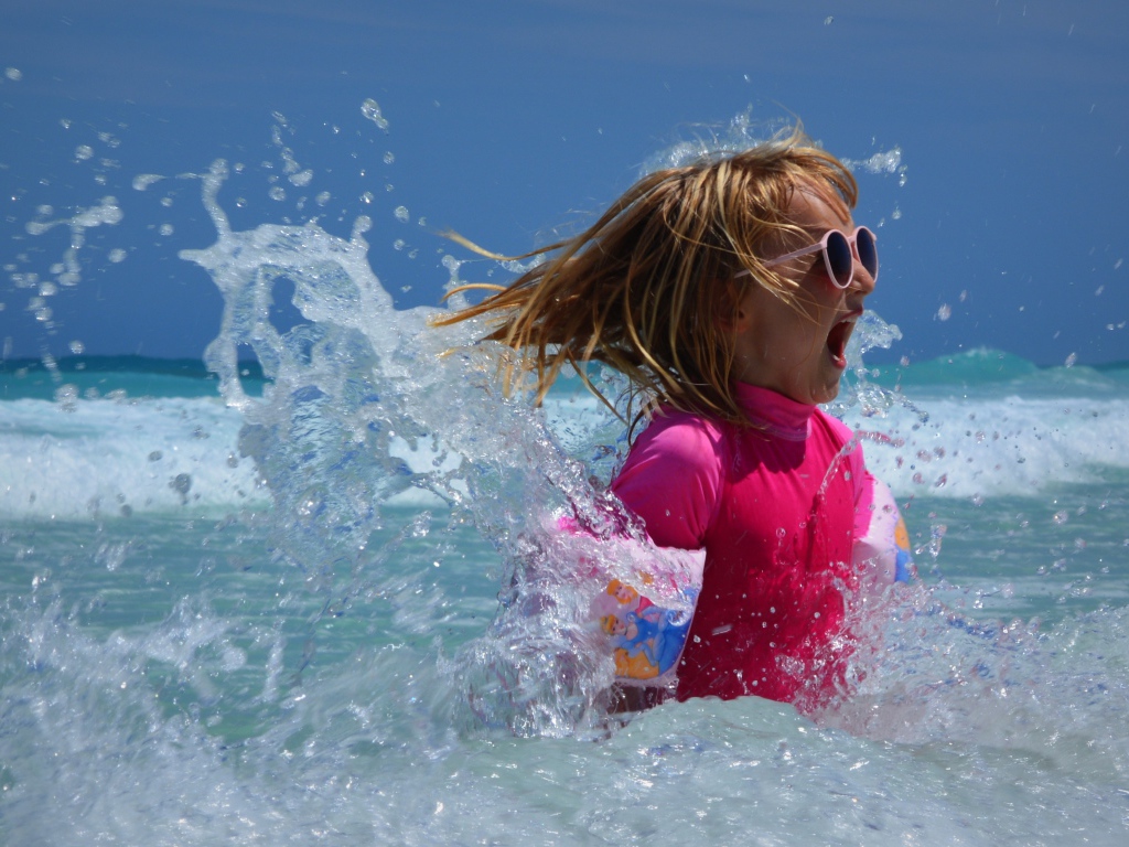 Веселая маленькая девочка купается в море летом