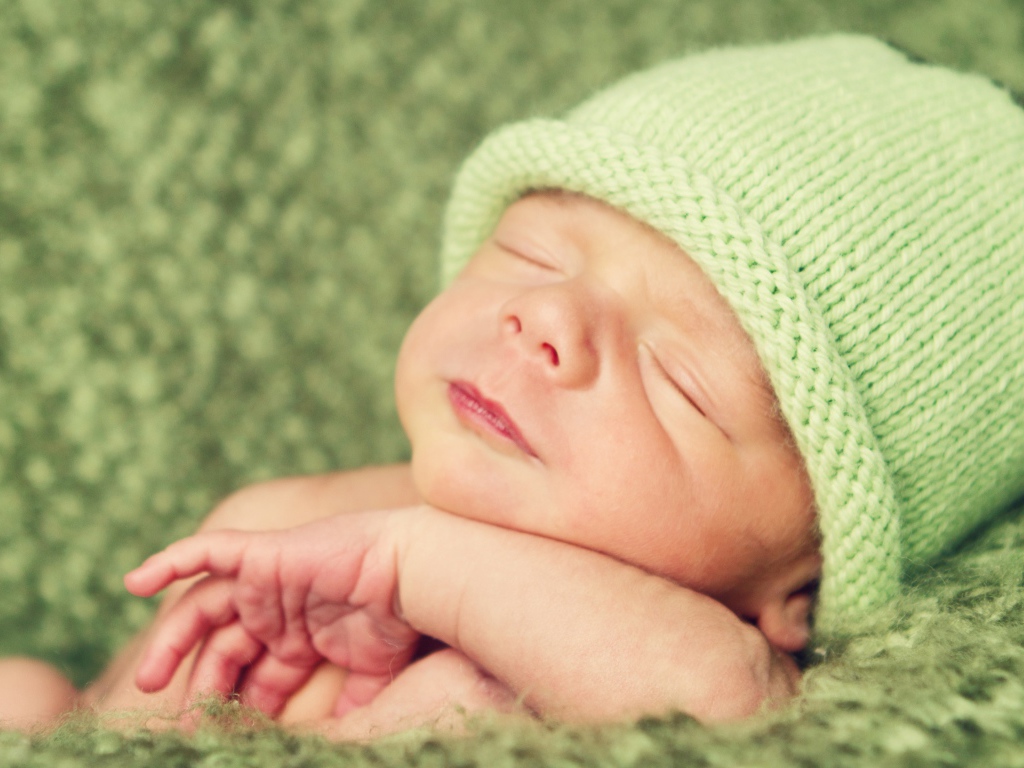 Зеленая вязаная шапка на голове у спящего ребенка 