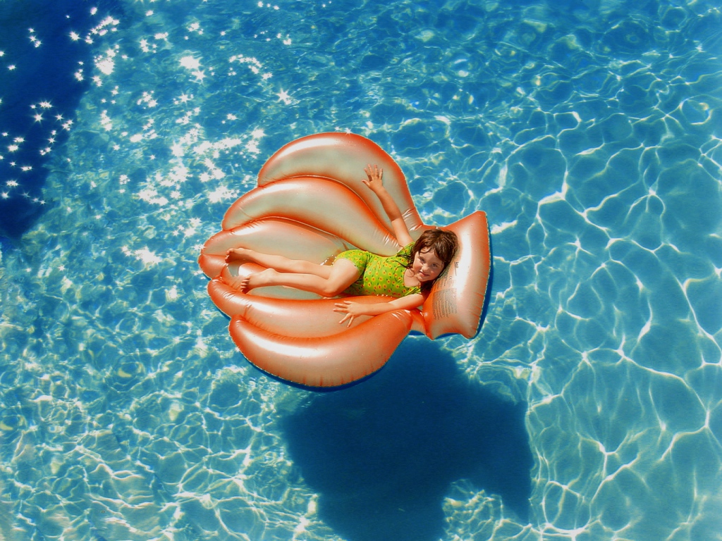 Маленькая девочка на надувном матрасе в бассейне летом 