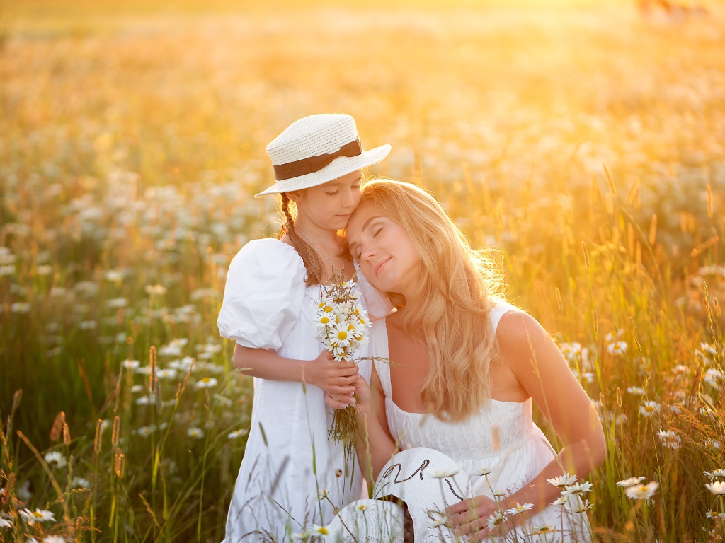 Мать с дочерью на поле с белыми ромашками в лучах солнца 