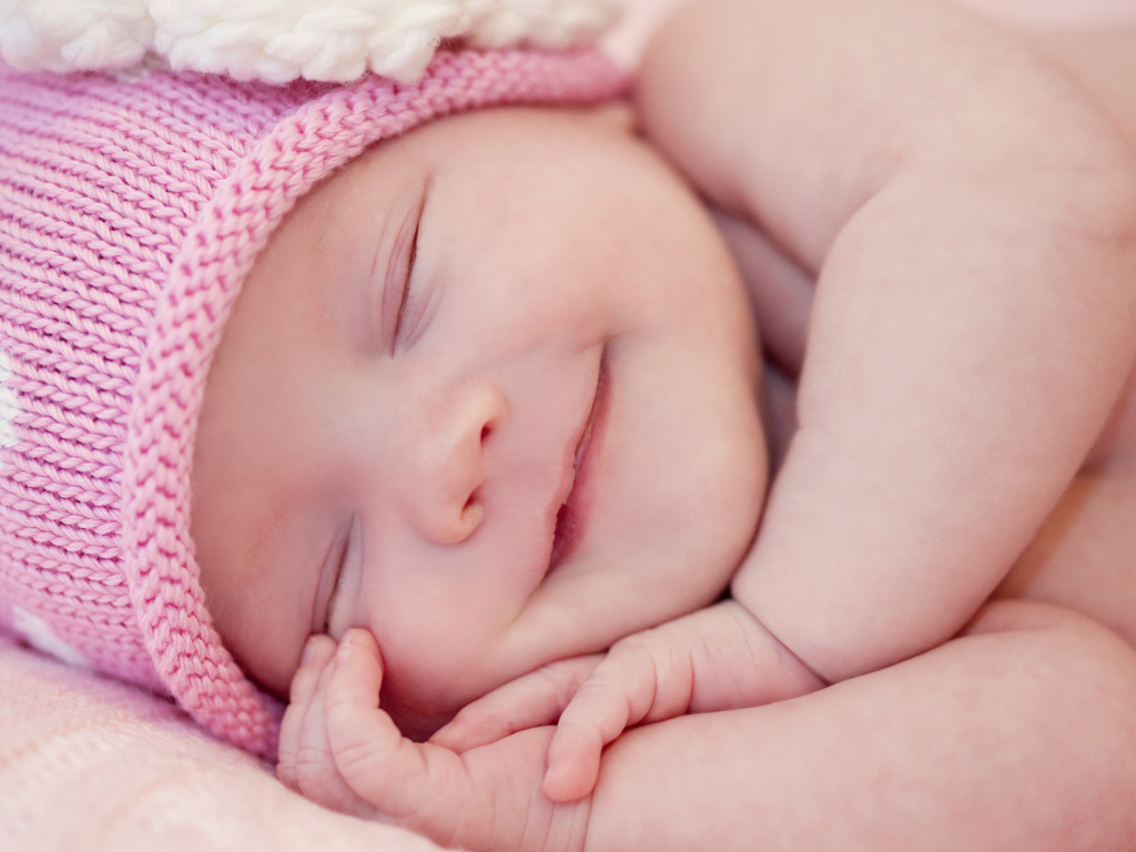 Улыбающийся грудной ребенок в розовой вязаной шапке 