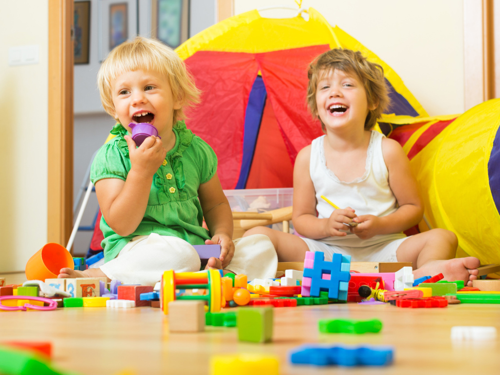 Два улыбающихся ребенка играют с конструктором 
