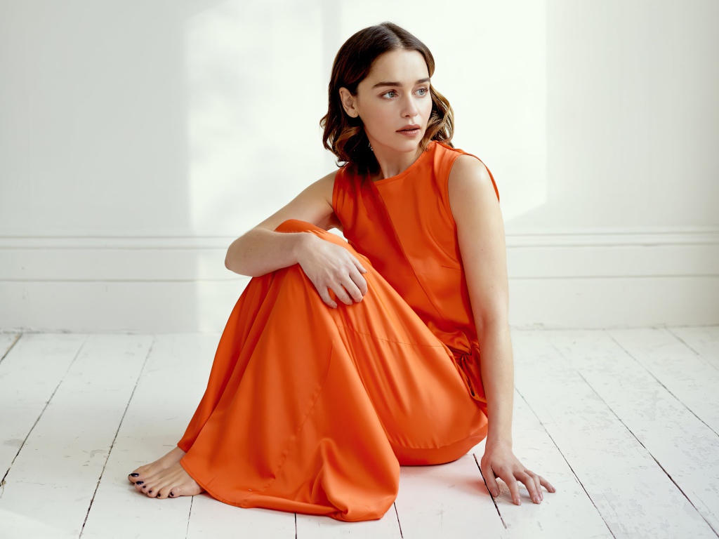 Актриса Эмилия Кларк  в оранжевом платье сидит на полу