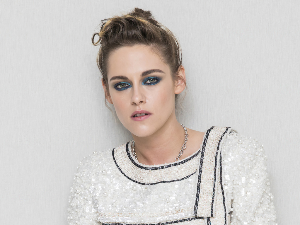 Актриса Кристен Стюарт с накрашенными глазами на фоне серой стены 