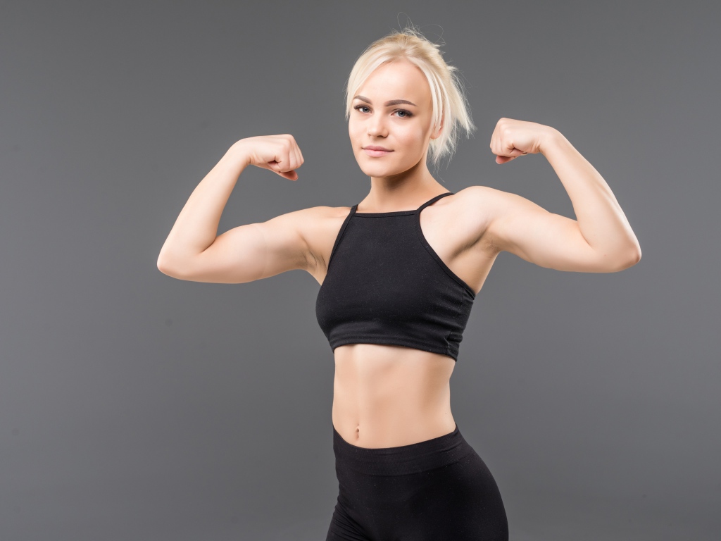 Красивая стройная спортивная девушка показывает мускулы