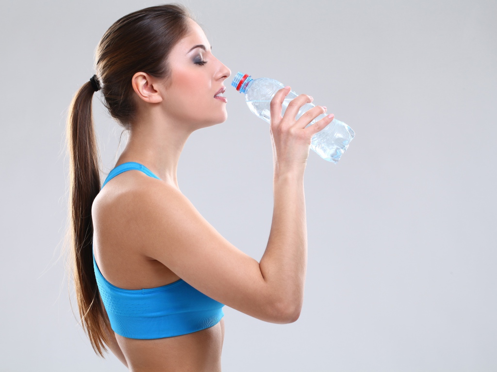 Красивая спортивная девушка пьет воду на сером фоне 