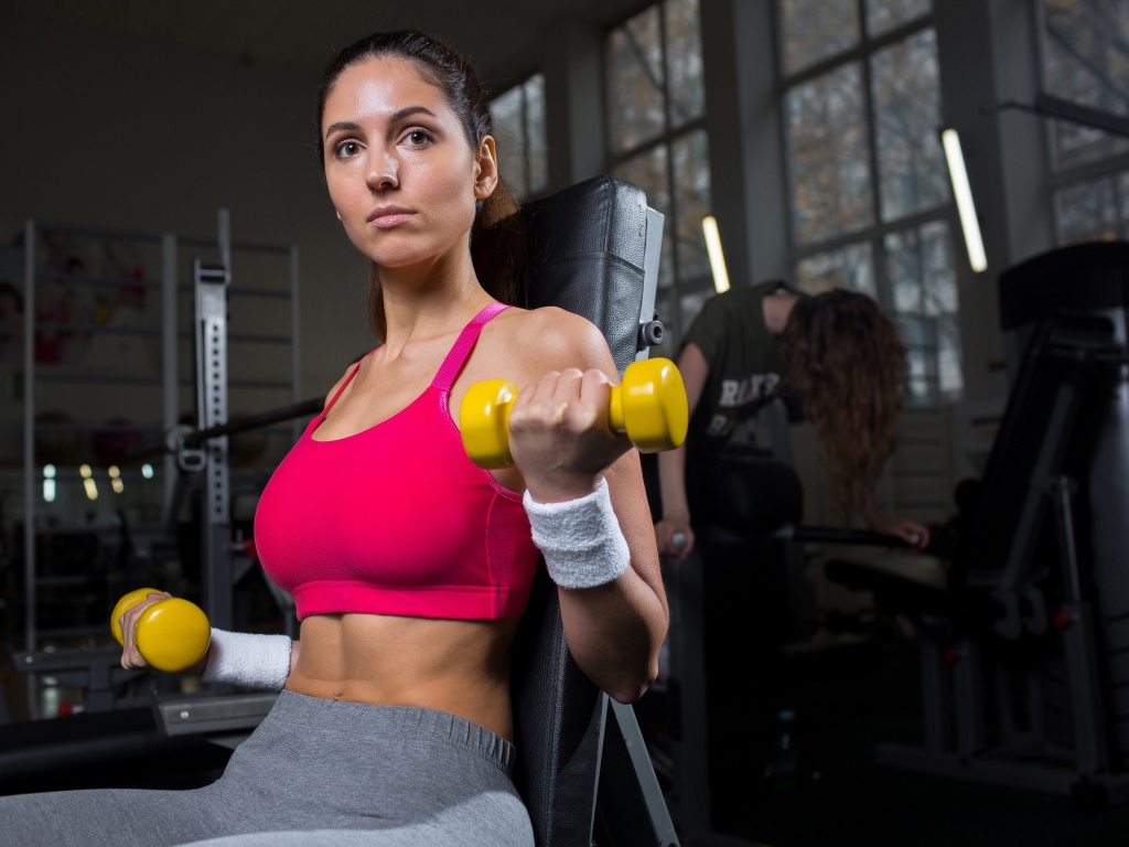 Спортивная девушка качает руки желтыми гантелями в спортзале