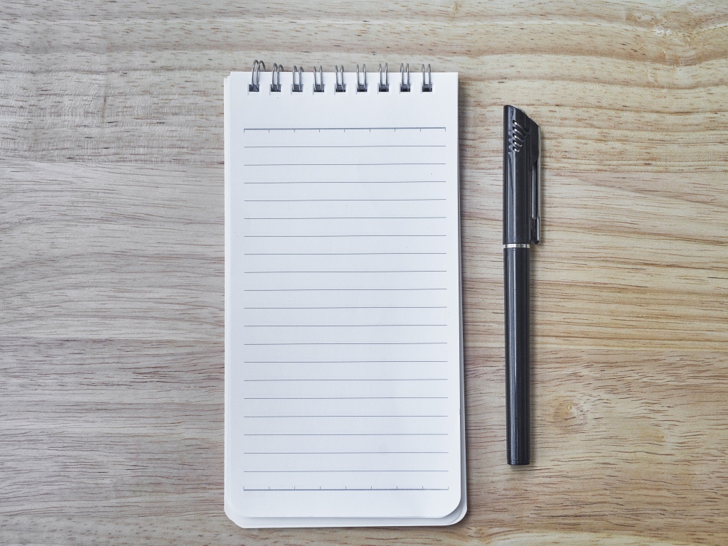 Авторучка и блокнот лежат на деревянном столе