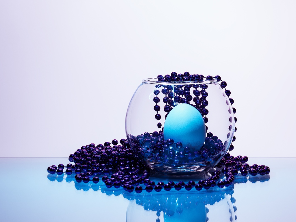 Синие бусы на столе со стеклянной вазой и яйцом