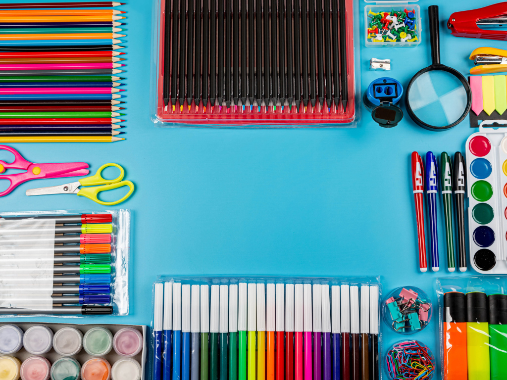 Много разноцветных канцелярских предметов на голубом фоне 