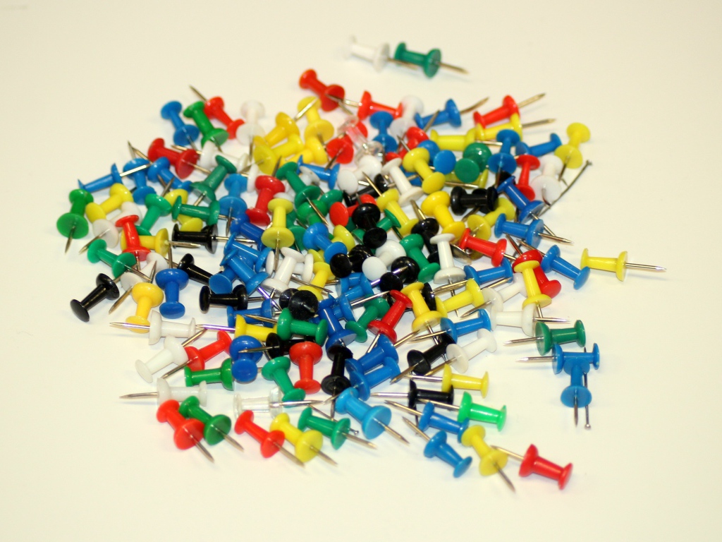 Разноцветные канцелярские гвозди на белом фоне