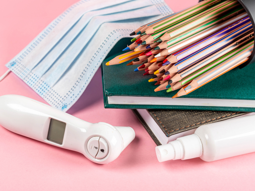 Карандаши, градусник, маска и блокнот на розовом фоне 