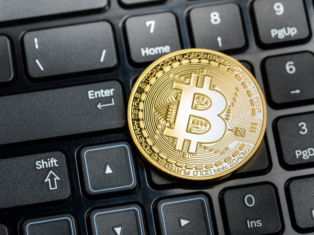 Золотая монета биткоин на черной клавиатуре