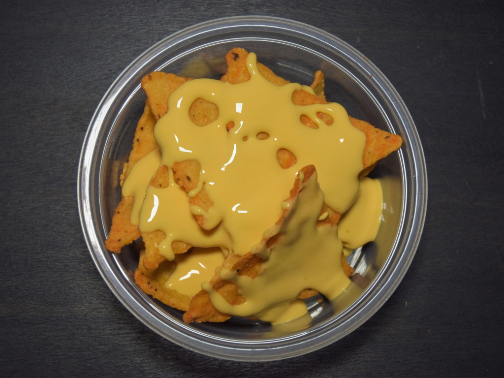 Чипсы начос с сырным соусом в миске на черном фоне