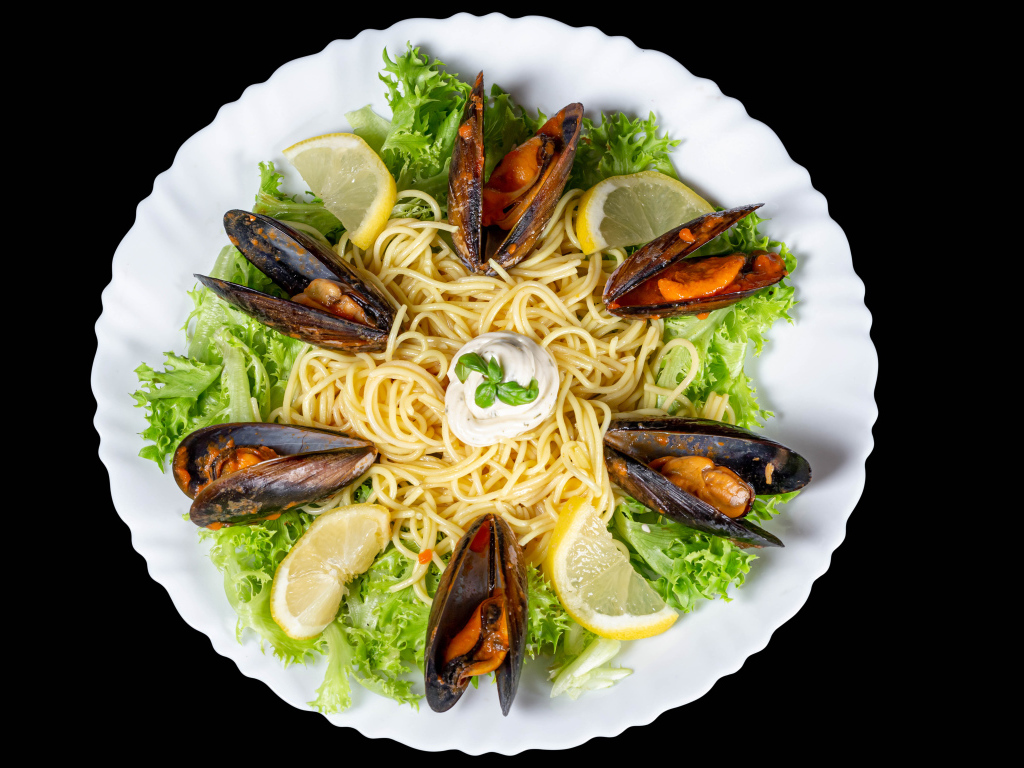 Спагетти с мидиями и листьями салата на белой тарелке