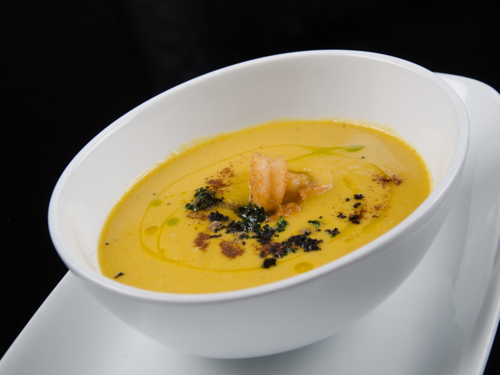 Желтый суп пюре в белой тарелке на черном фоне