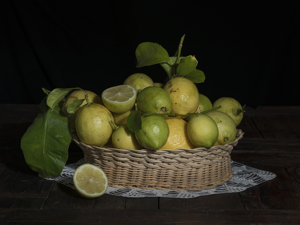 Lemons and limes in a wicker basket on a black background