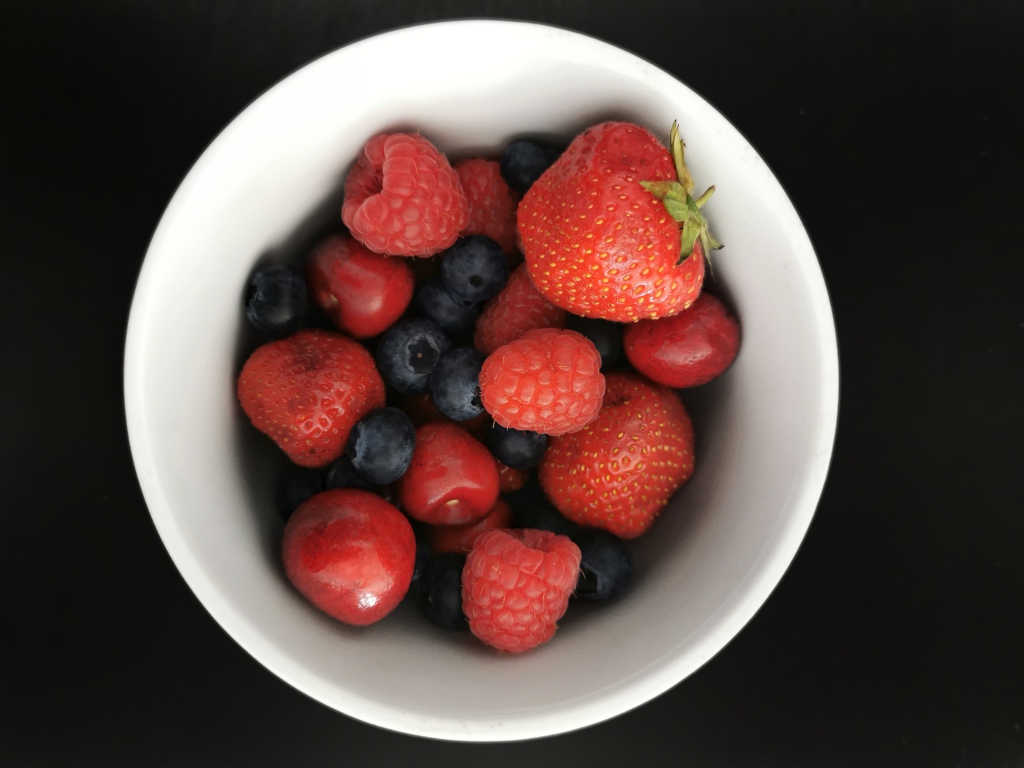 Спелые свежие ягоды в белой тарелке на белом фоне