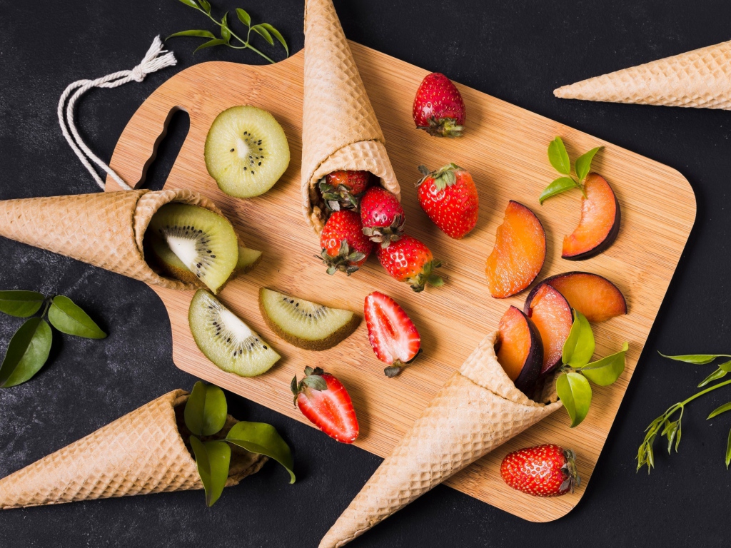 Вафельные рожки с ягодами и фруктами на доске 