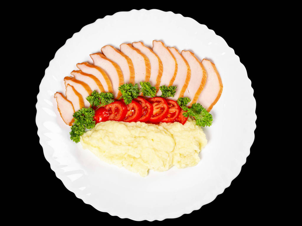 Ham on a large white plate with potatoes and tomatoes