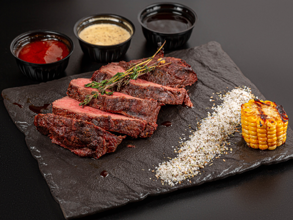 Кусок запеченного мяса на доске с кукурузой и специями 