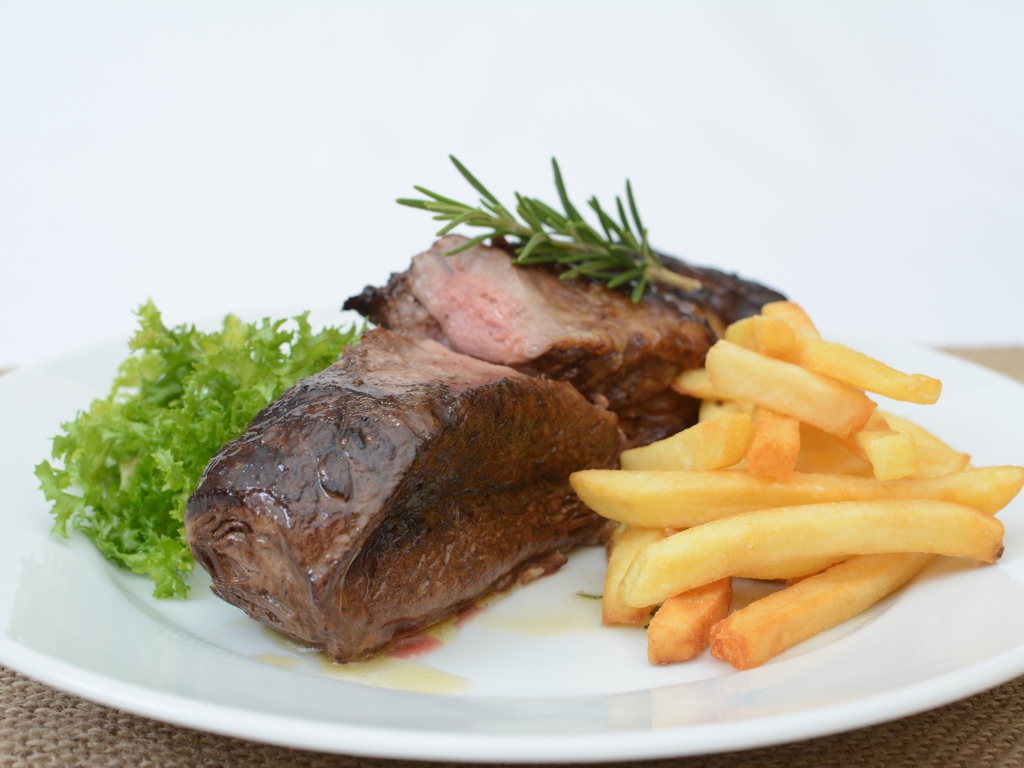 Два куска мяса на тарелке с картофелем фри 