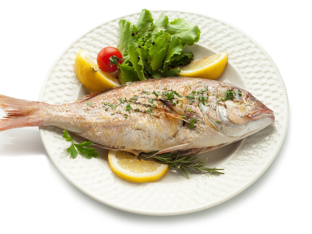 Запеченная рыба на тарелке с зеленью и лимоном