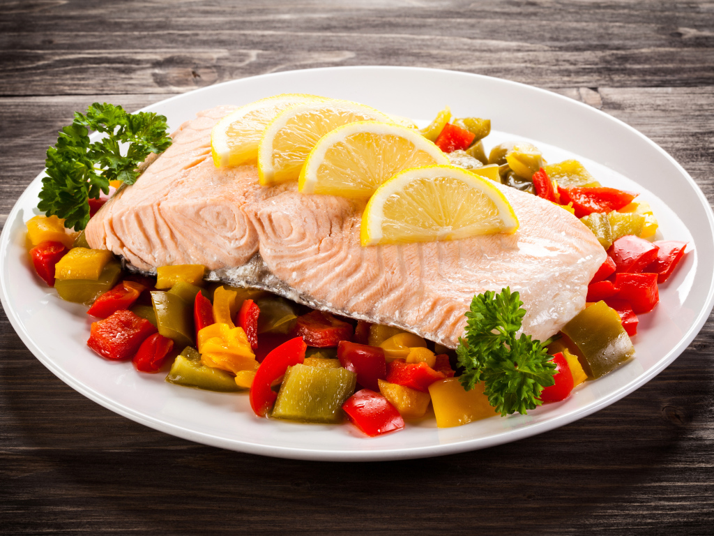 Кусок рыбы на тарелке с овощами и лимоном