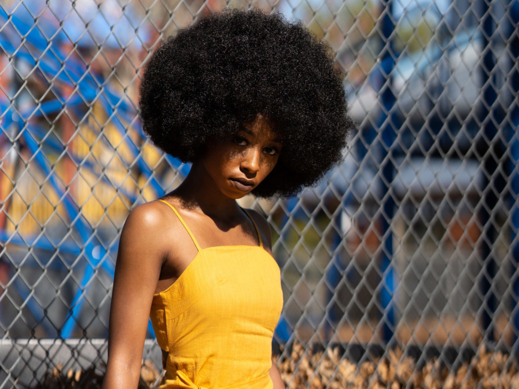Темнокожая девушка в желтом платье стоит у сетки