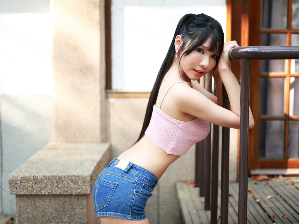 Девушка азиатка в коротких шортах стоит у перил 