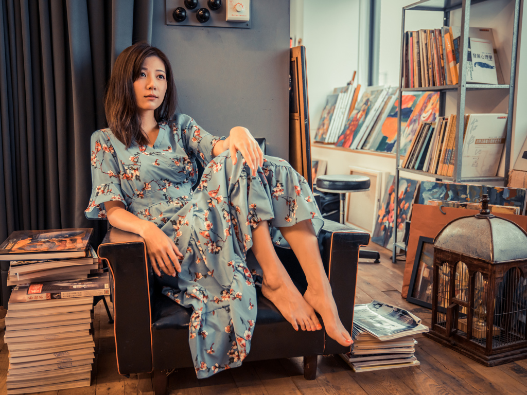 Девушка азиатка сидит в большом кресле в комнате с книгами