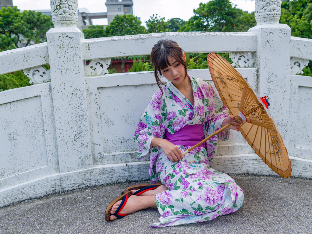 Девушка азиатка сидит в кимоно с зонтом 