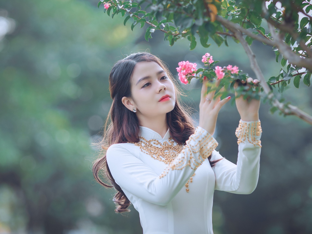 Красивая азиатка в белом платье у ветки с розовыми цветами