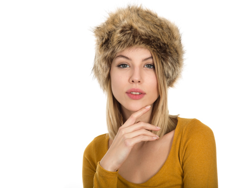 Красивая девушка блондинка в меховой шапке на белом фоне 