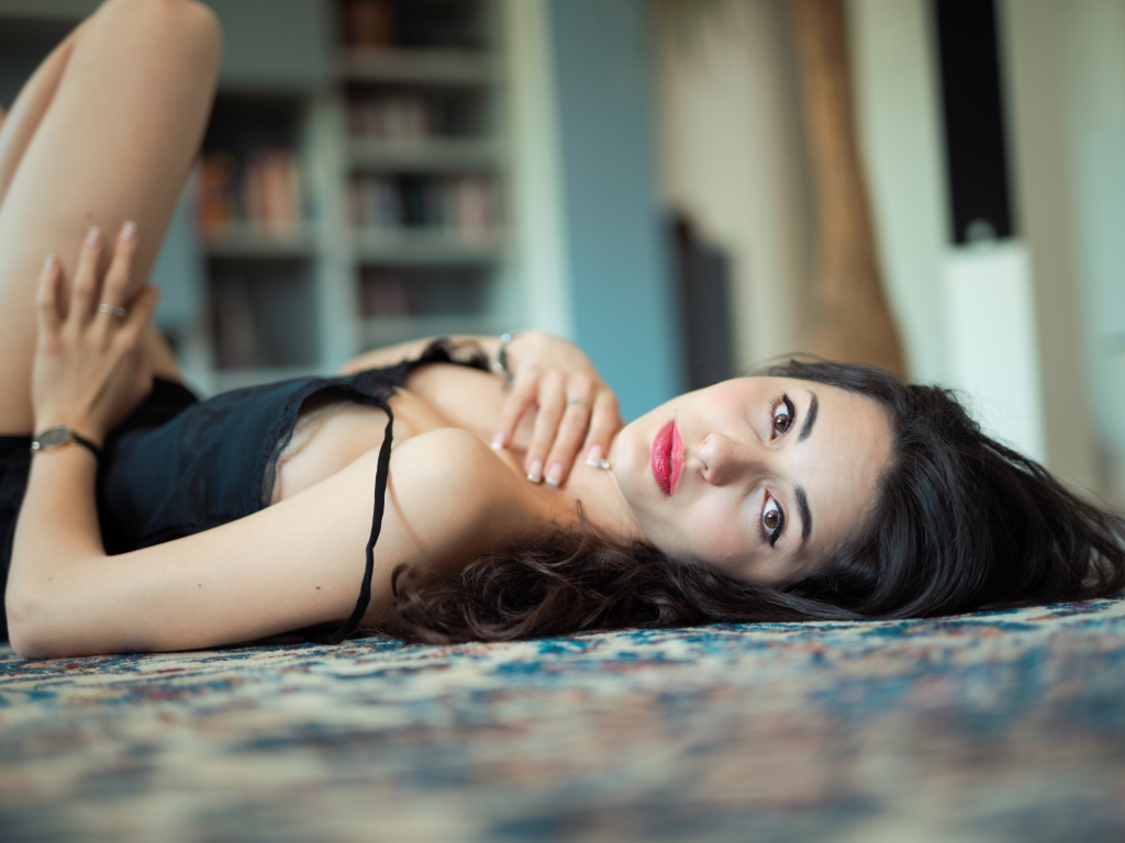 Красивая брюнетка в черном платье лежит на полу