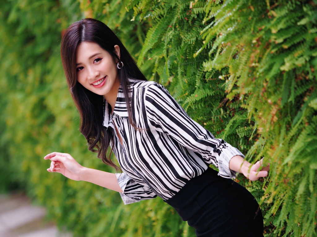 Красивая девушка в полосатой рубашке стоит у растения