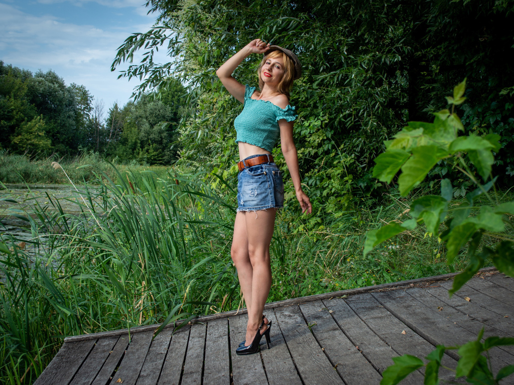 Красивая девушка в джинсовой юбке у пруда 