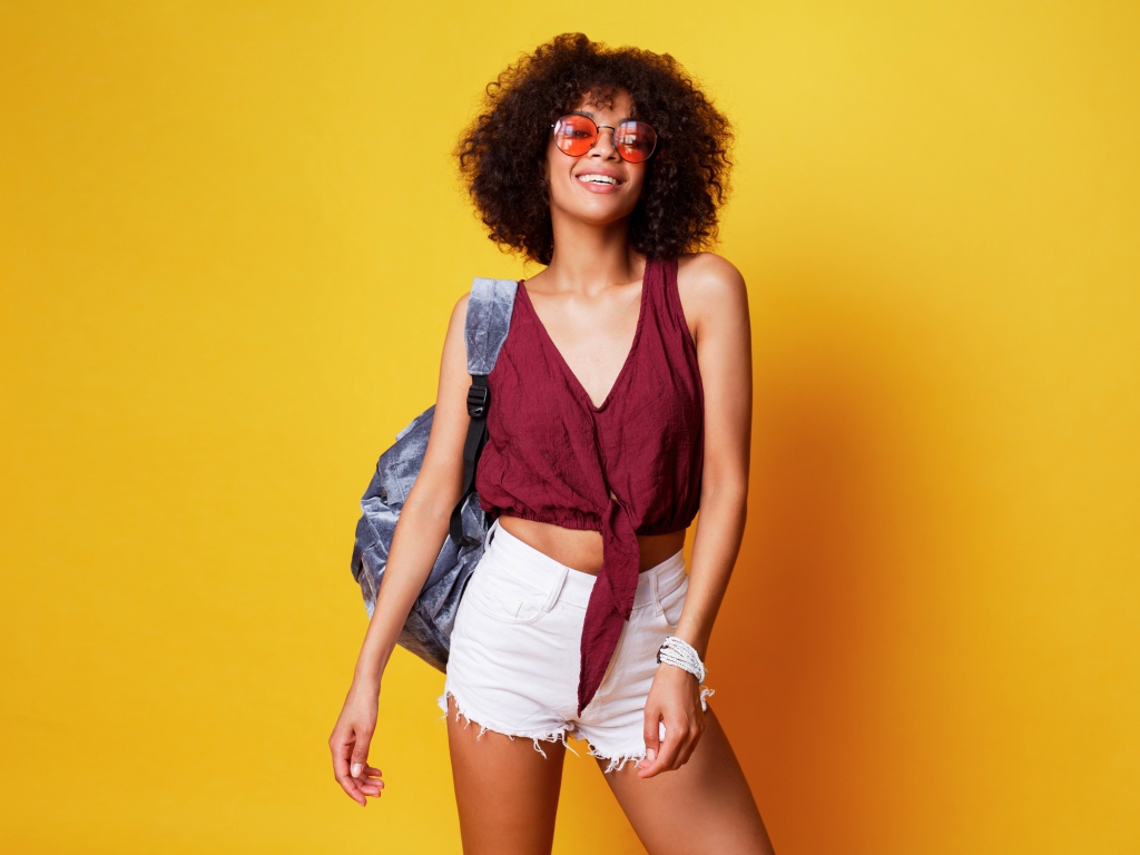 Красивая девушка в очках с рюкзаком на желтом фоне 