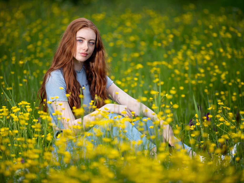 Голубоглазая девушка сидит на поле с желтыми цветами