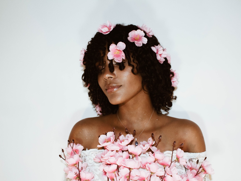 Темнокожая девушка в розовых цветах на сером фоне