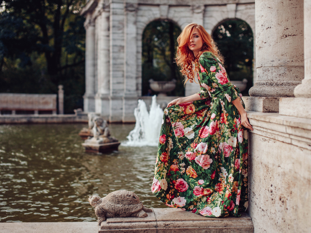 Девушка в красивом цветастом платье у пруда в парке 
