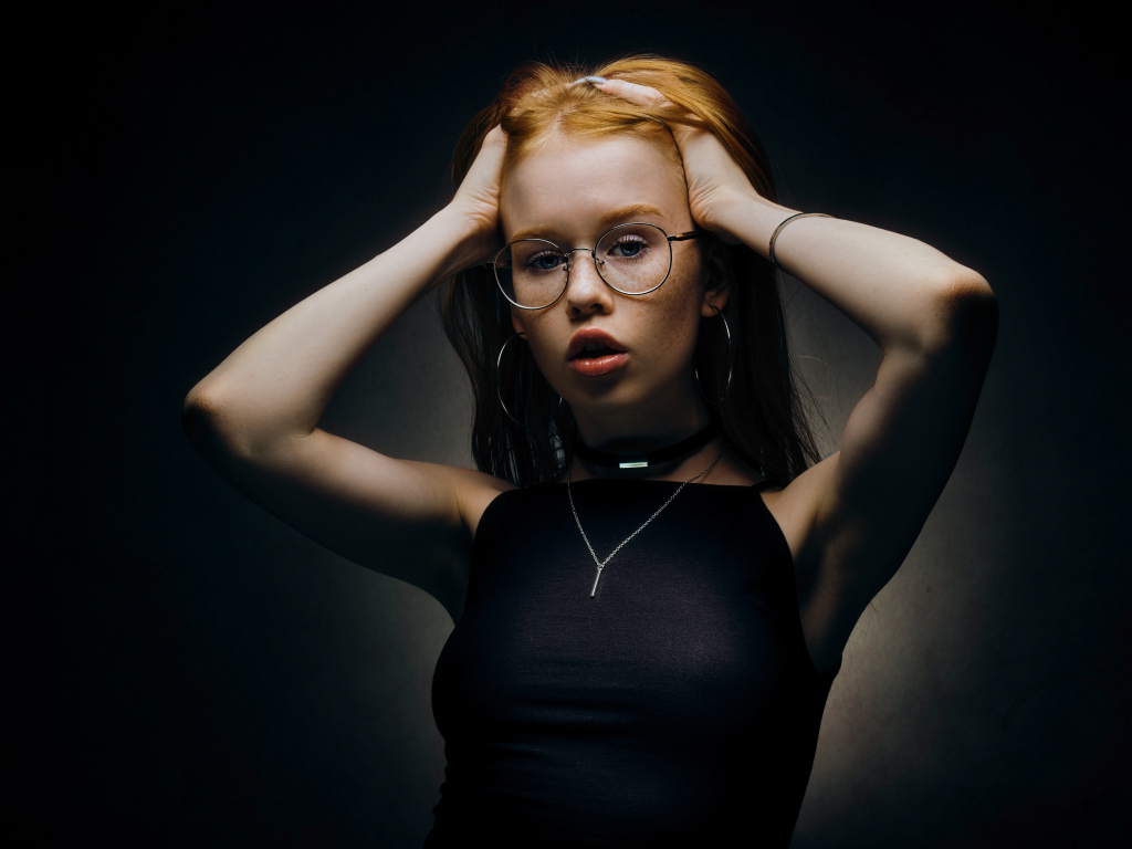 Рыжеволосая девушка в очках на черном фоне