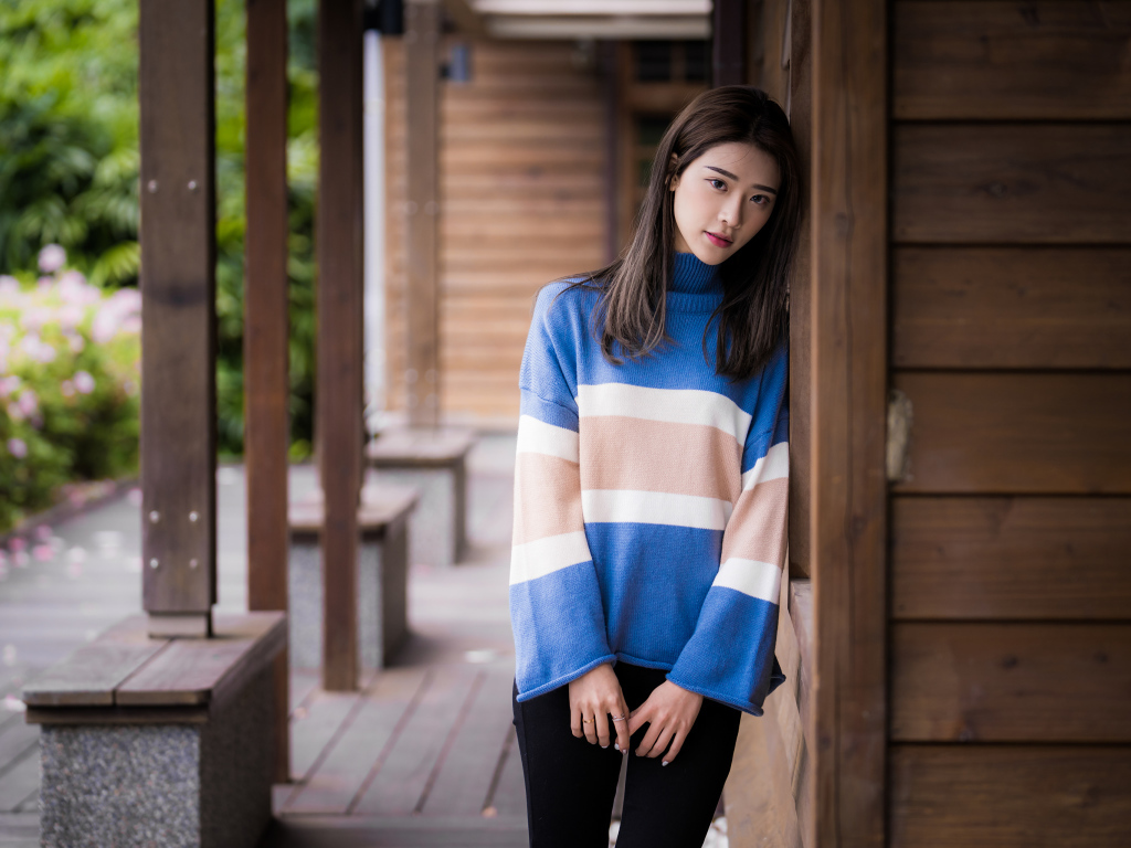 Грустная девушка азиатка в свитере у стены 