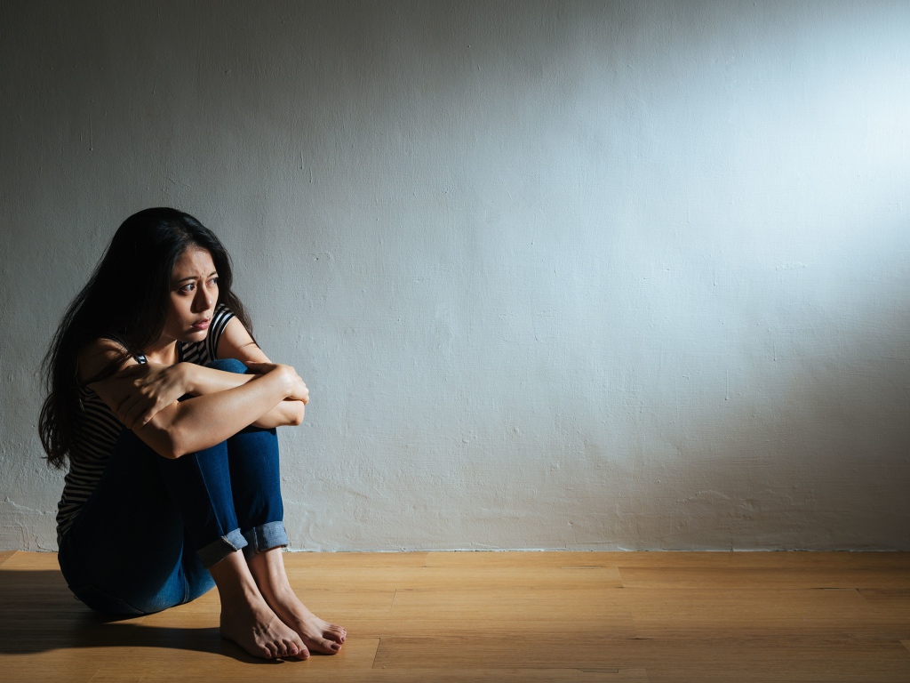 Испуганная девушка азиатка сидит у стены