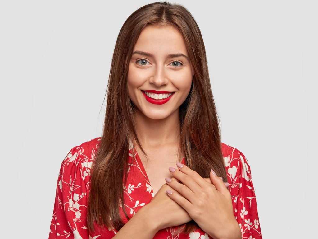 Улыбающаяся девушка с руками на сердце на сером фоне