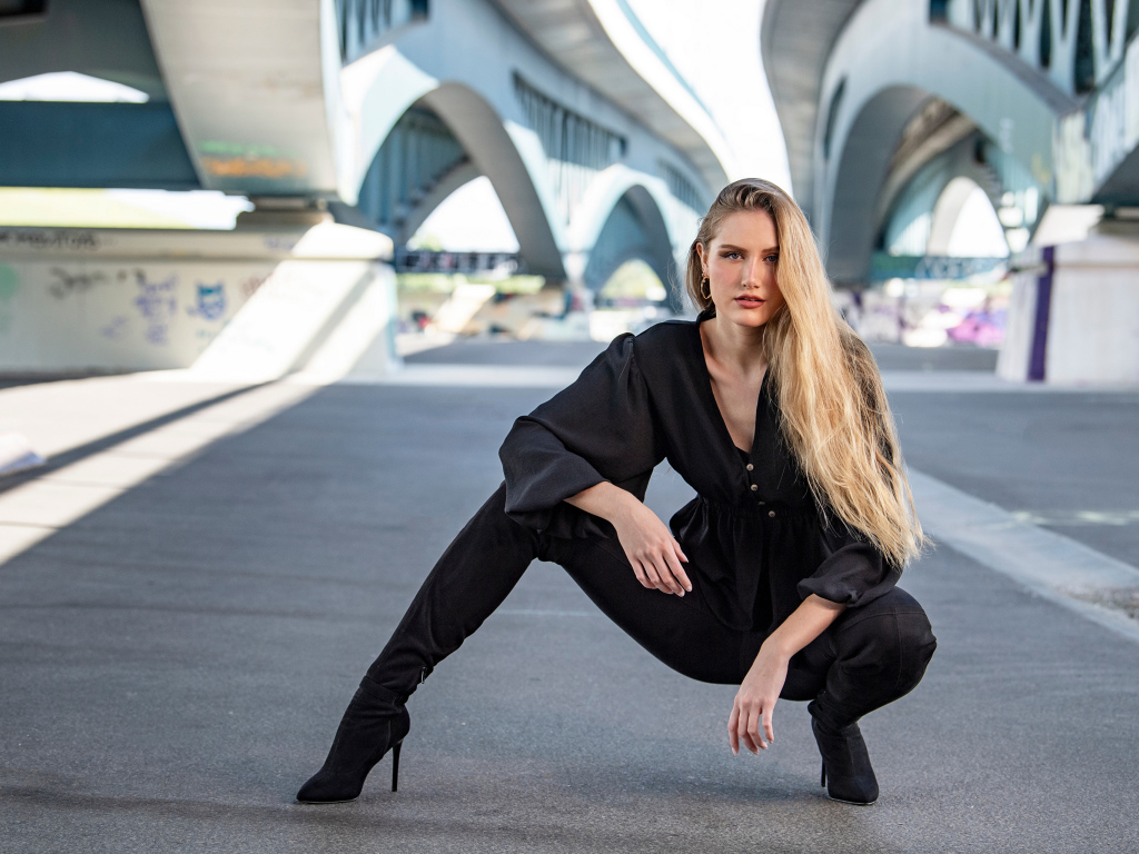 Стильная девушка в черном костюме под мостом