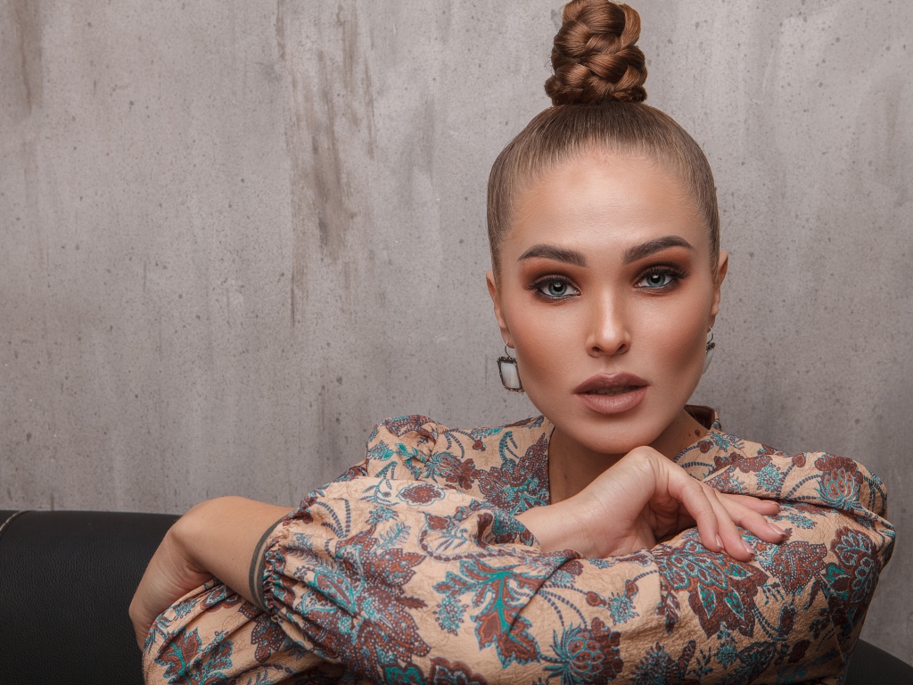 Молодая девушка с прической на голове на фоне стены